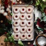 Gluten-Free Linzer Cookies with raspberry jam and a dusting of powdered sugar on a beige plate.