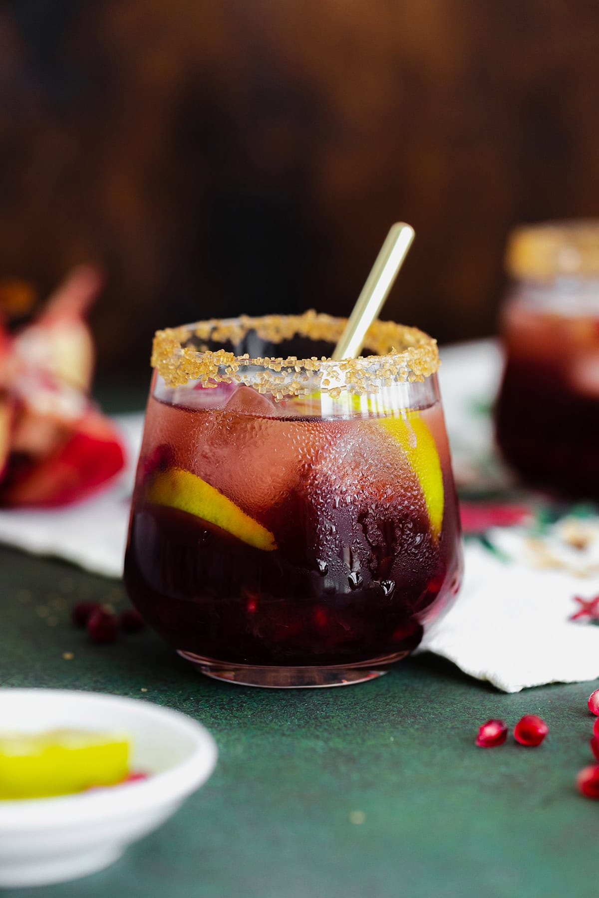 Pomegranate Margarita in a short glass and coarse sugar on the rim. On a christmas themed tea towel and a dark wooden background.