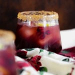 Pomegranate Margarita in a short glass and coarse sugar on the rim. On a christmas themed tea towel and a dark wooden background.