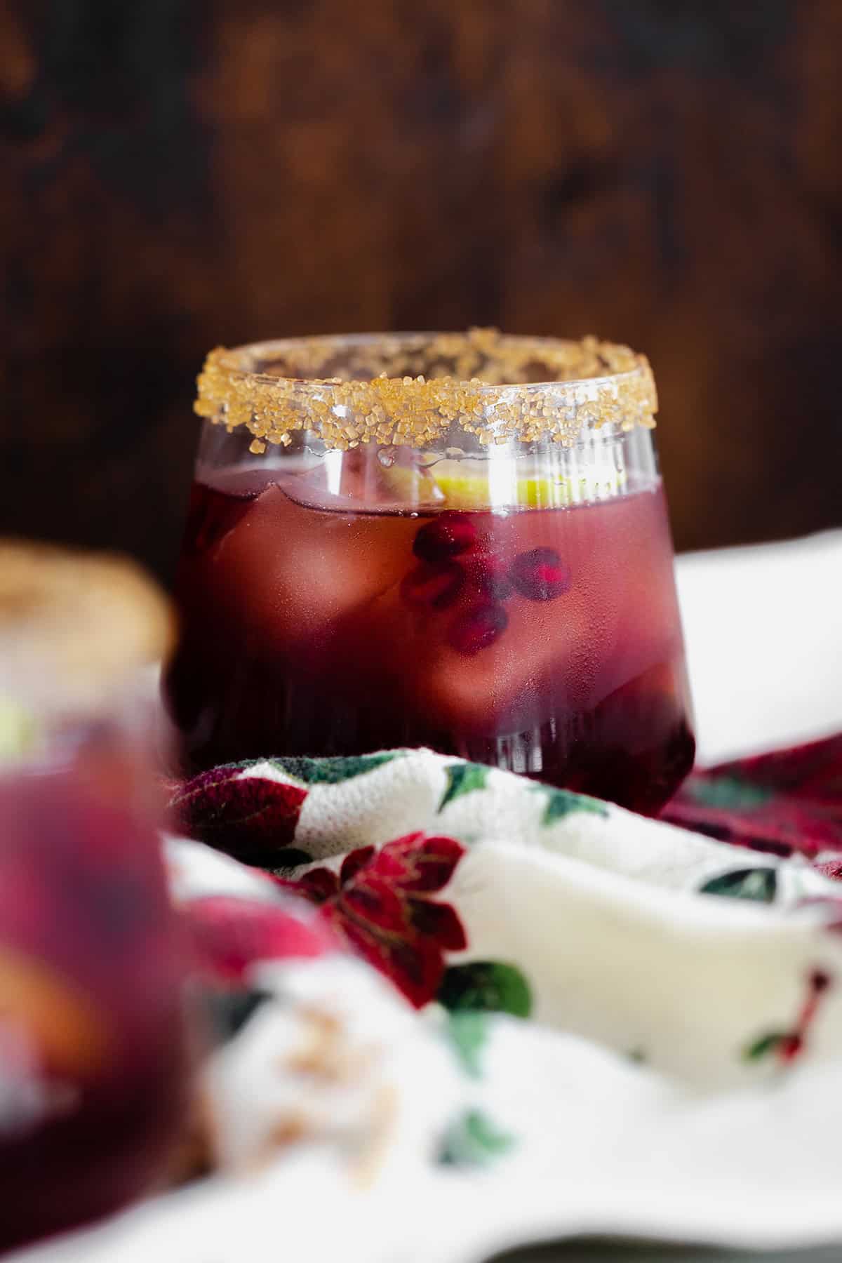 Pomegranate Margarita in a short glass and coarse sugar on the rim. On a christmas themed tea towel and a dark wooden background.