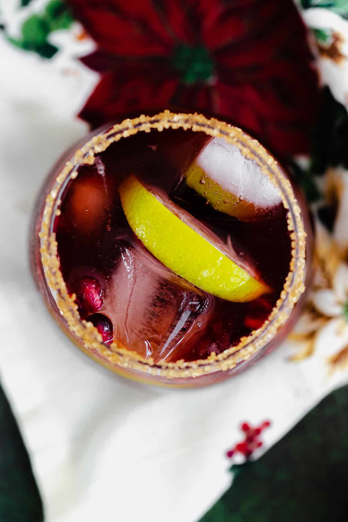 Pomegranate Margarita in a short glass and coarse sugar on the rim. On a christmas themed tea towel and a dark wooden background.