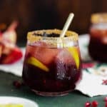 Pomegranate Margarita in a short glass and coarse sugar on the rim. On a christmas themed tea towel and a dark wooden background.