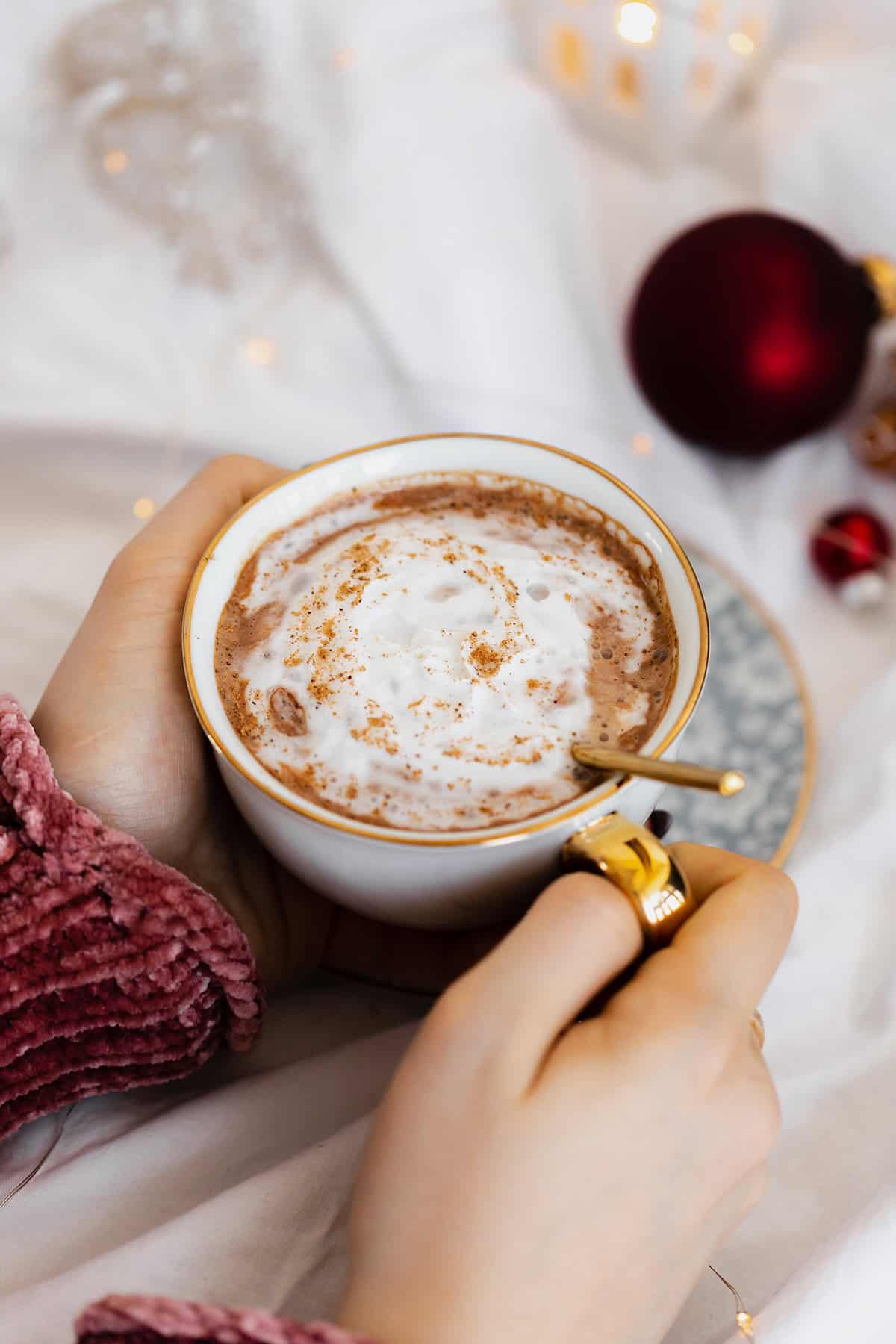 Vegan Eggnog Mocha with whipped cream and a sprinkle of nutmeg in a white mug on white bedsheets.