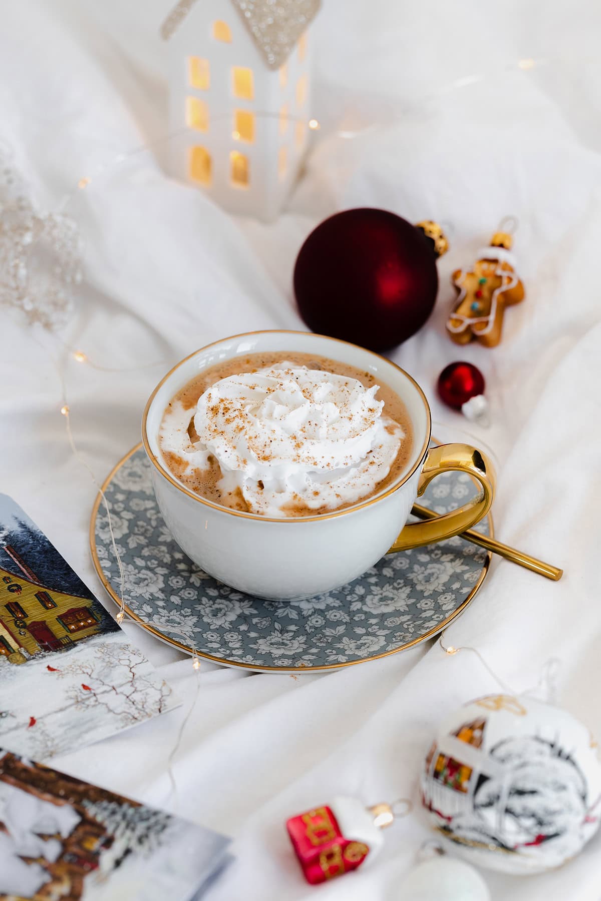 Vegan Eggnog Mocha with whipped cream and a sprinkle of nutmeg in a white mug on white bedsheets.