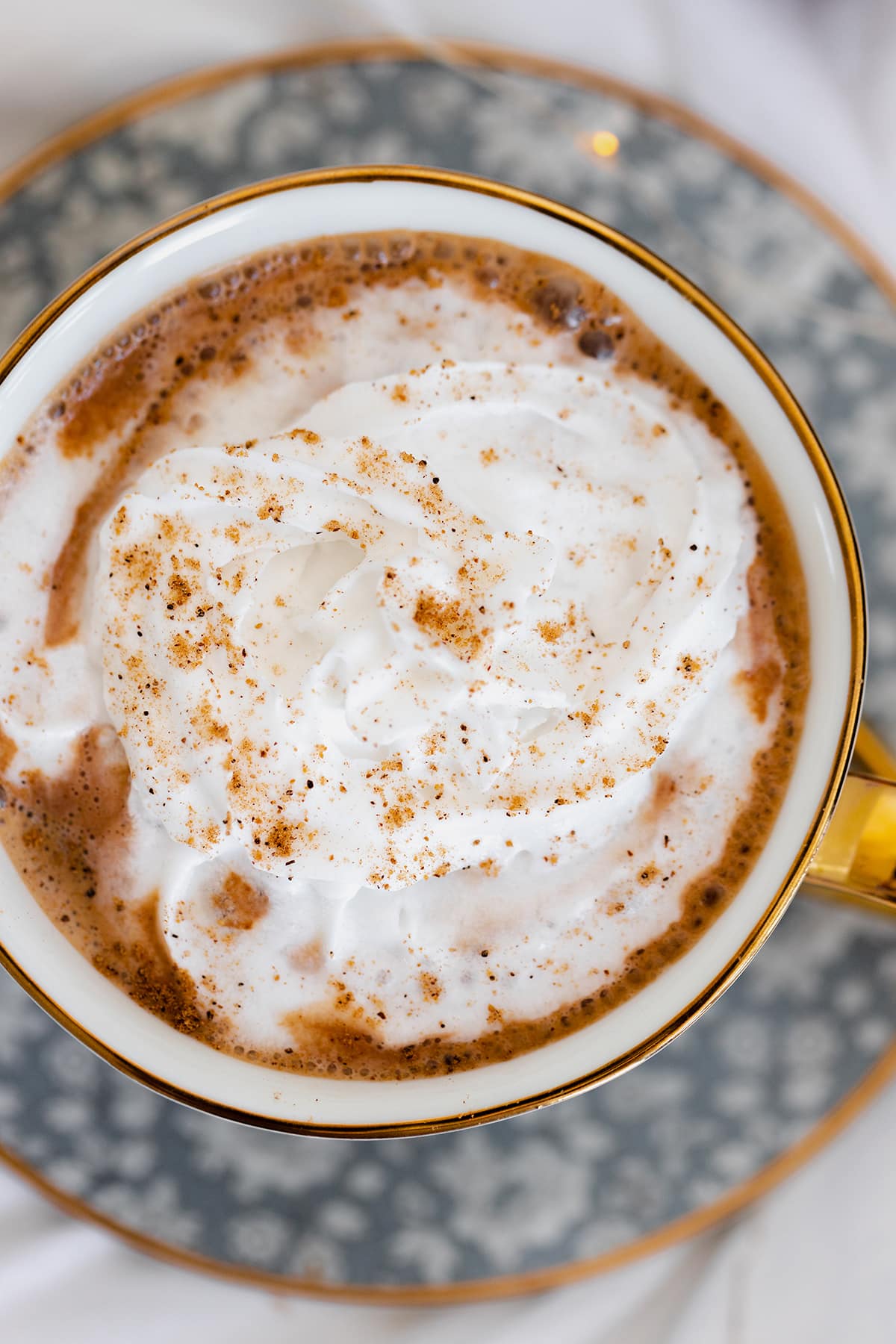 Vegan Eggnog Mocha with whipped cream and a sprinkle of nutmeg in a white mug on white bedsheets.