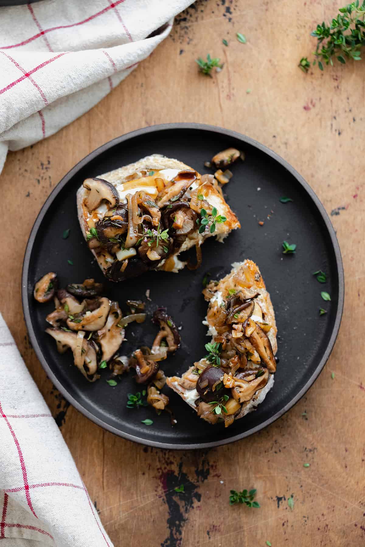 Whipped Goat Cheese Toast with Shiitake Mushroom on a black plate and a light wooden table. Natural cotton napkin on the left side.