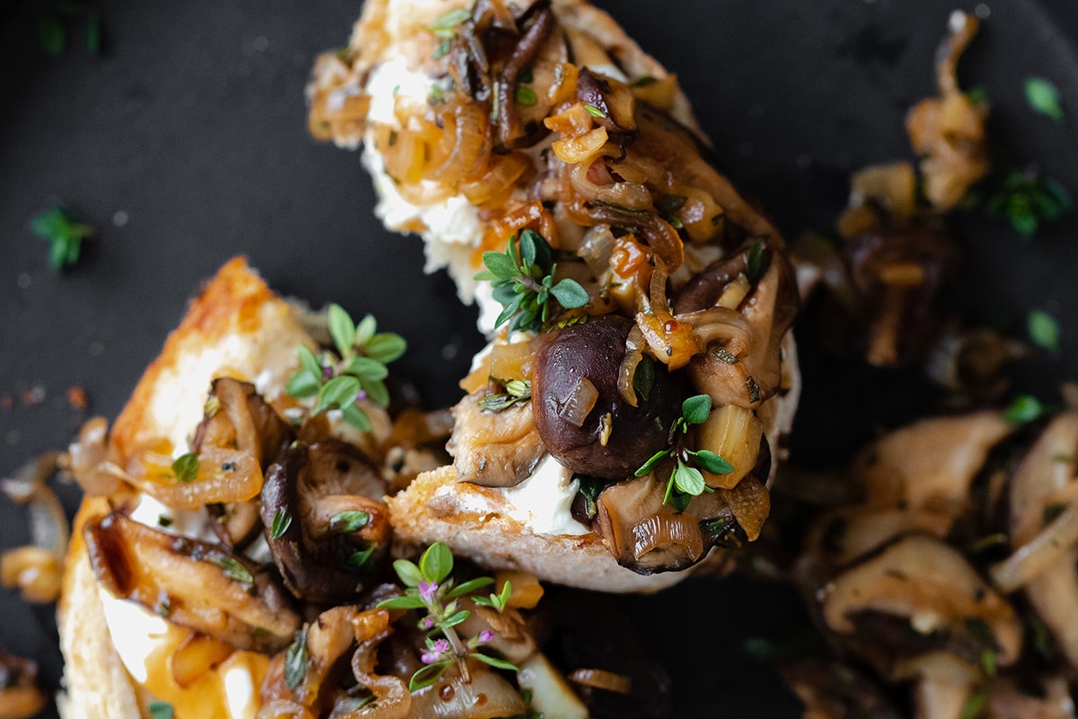 Whipped Goat Cheese Toast with Shiitake Mushroom on a black plate and a light wooden table.