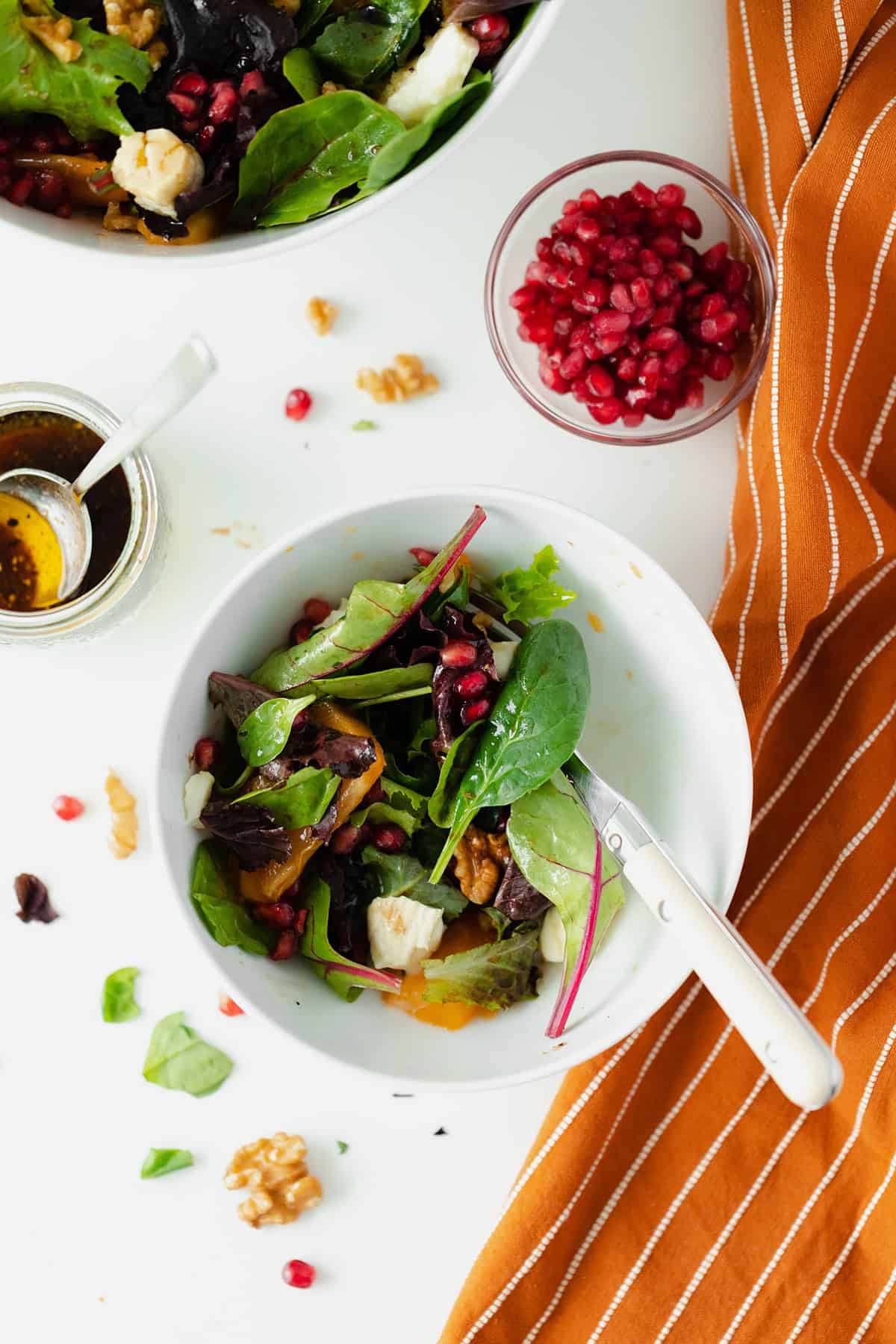 Persimmon Salad with Goat Brie and Pomegranate seeds in a white bowl on a white background with an orange napkin on the right side