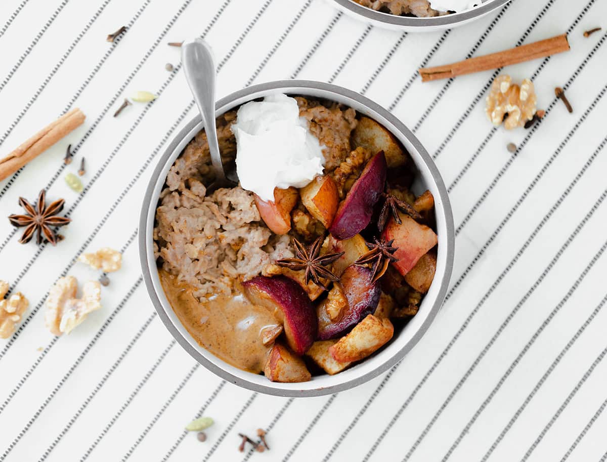 Winter Spiced Oatmeal with Roasted Fruit on a white tablecloth with black stripes.