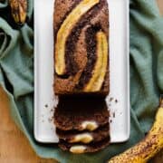 A photo of Caramelized Chocolate Banana Bread on a beige plate, green kitchen towel, and light wooden table.