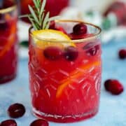 Cranberry Orange Margarita in a glass with a gold rim on a blue table with a black background.