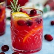 Cranberry Orange Margarita in a glass with a gold rim on a blue table with a black background.