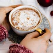 Vegan Eggnog Mocha with whipped cream and a sprinkle of nutmeg in a white mug on white bedsheets.
