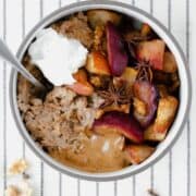 Winter Spiced Oatmeal with Roasted Fruit on a white tablecloth with black stripes.