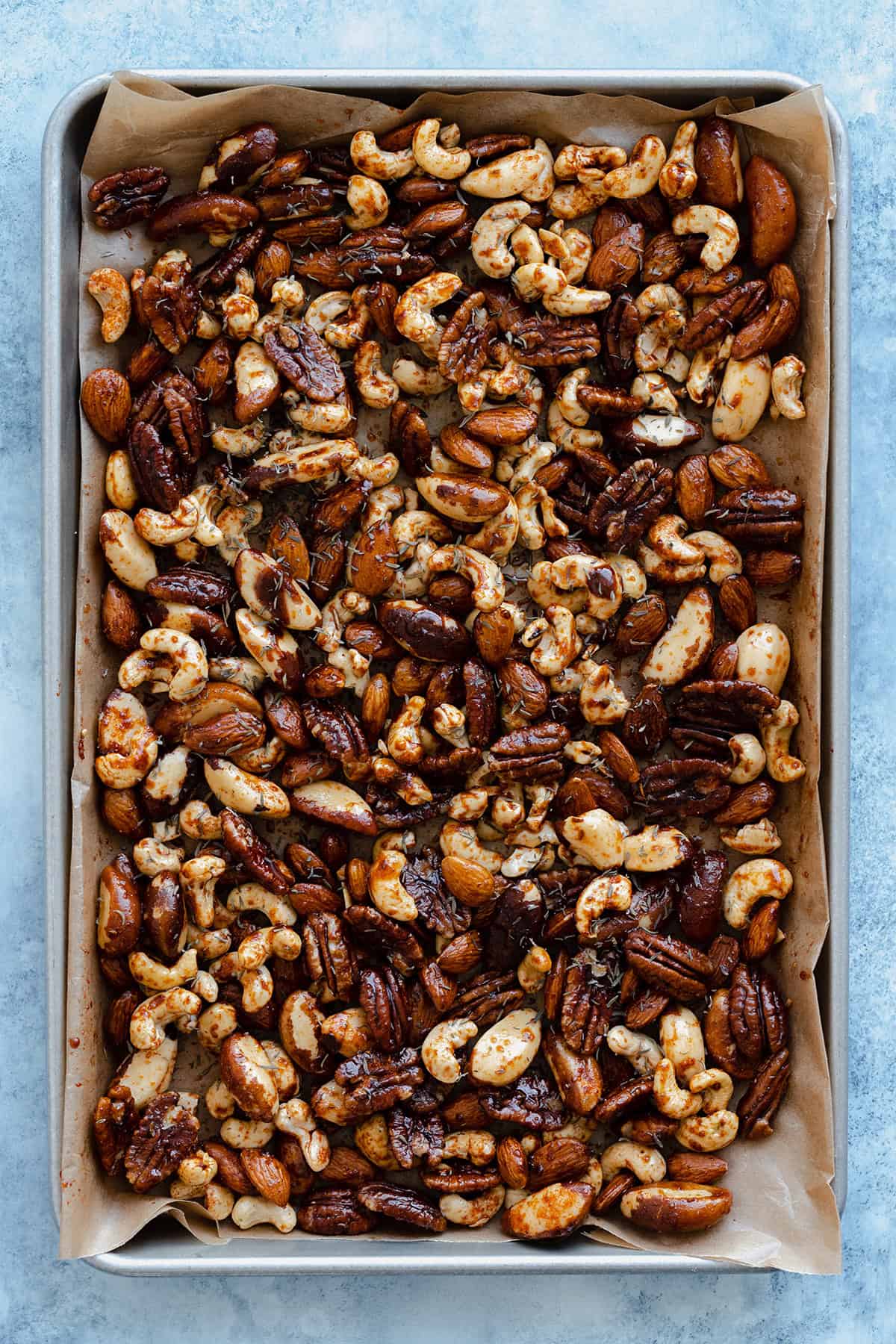 Raw nuts tossed in oil, maple syrup, and cajun spice on a baking sheet lined with baking paper.