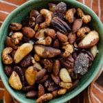 A close-up shot of roasted nuts in a green bowl on an orange and white striped napkin.