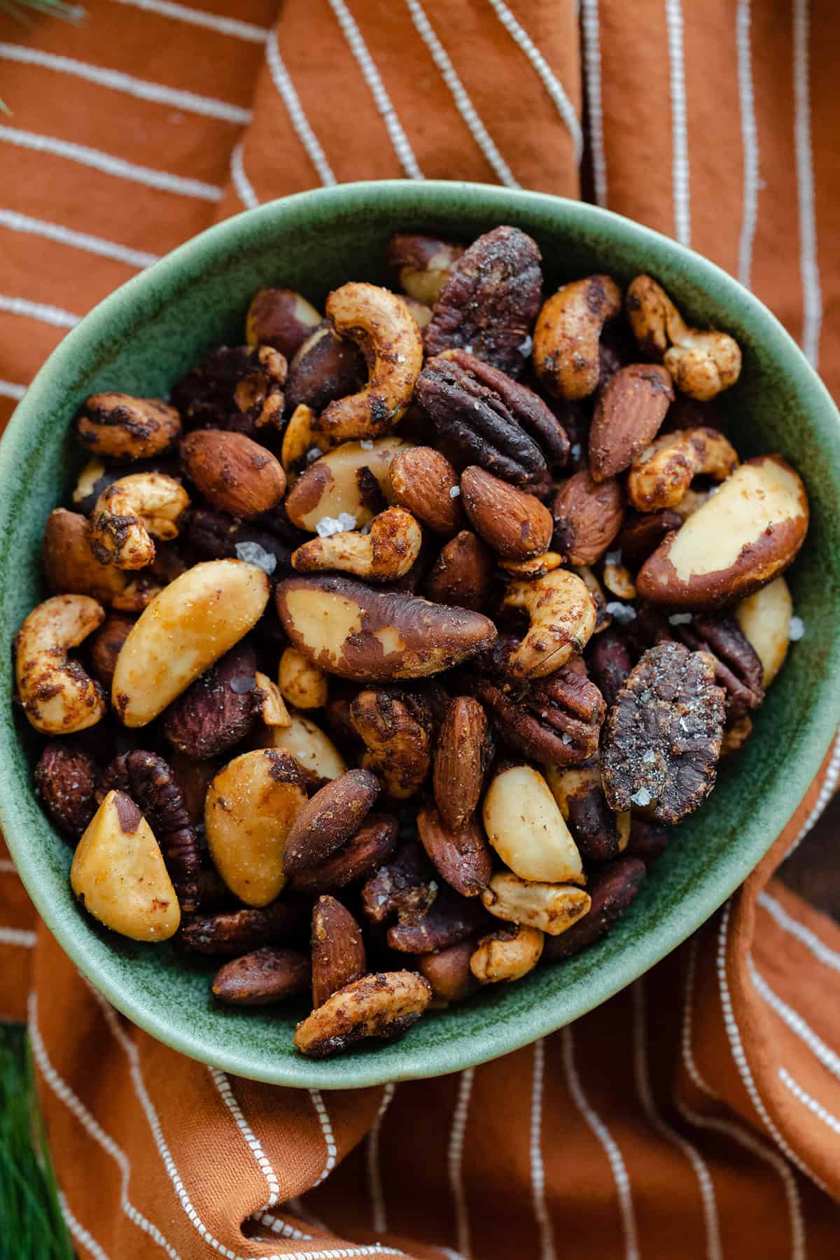 A close-up shot of roasted nuts in a green bowl on an orange and white striped napkin.