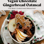 Gingerbread oatmeal with the title in the shot. In a beige bowl garnished with sliced pear, a slice of apple, a few blueberries, and two gingrbread men. On light wooden background with a Christmas tea towel under the bowl.