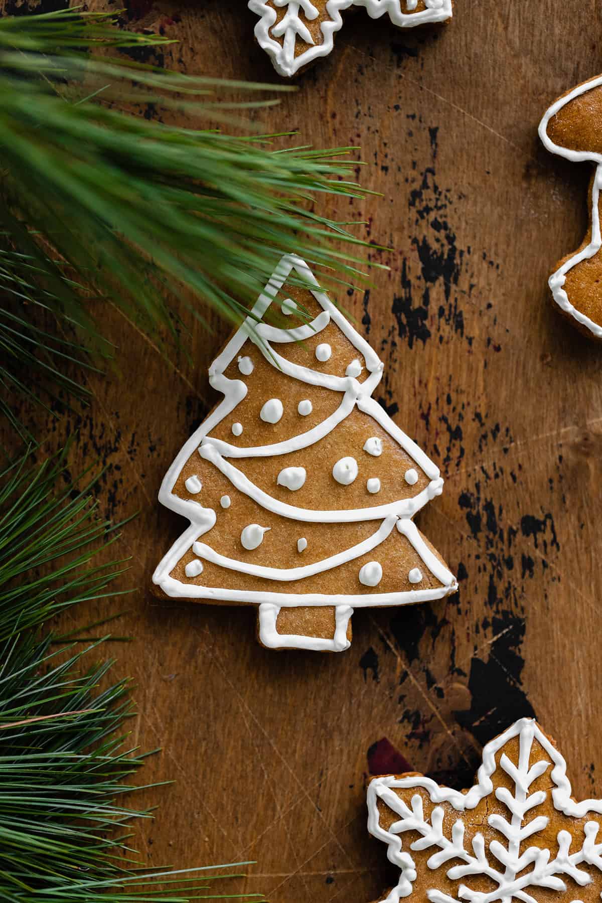 A close up of a Christmas tree shaped gingerbread cookie on a light wooden background. Decorated with white icing.