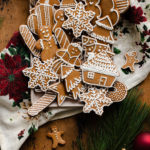 Czech Gingerbread Cookies on a plate with a Christmas tea towel underneath. On a light wooden background with pine branches and Christmas decorations around the plate.