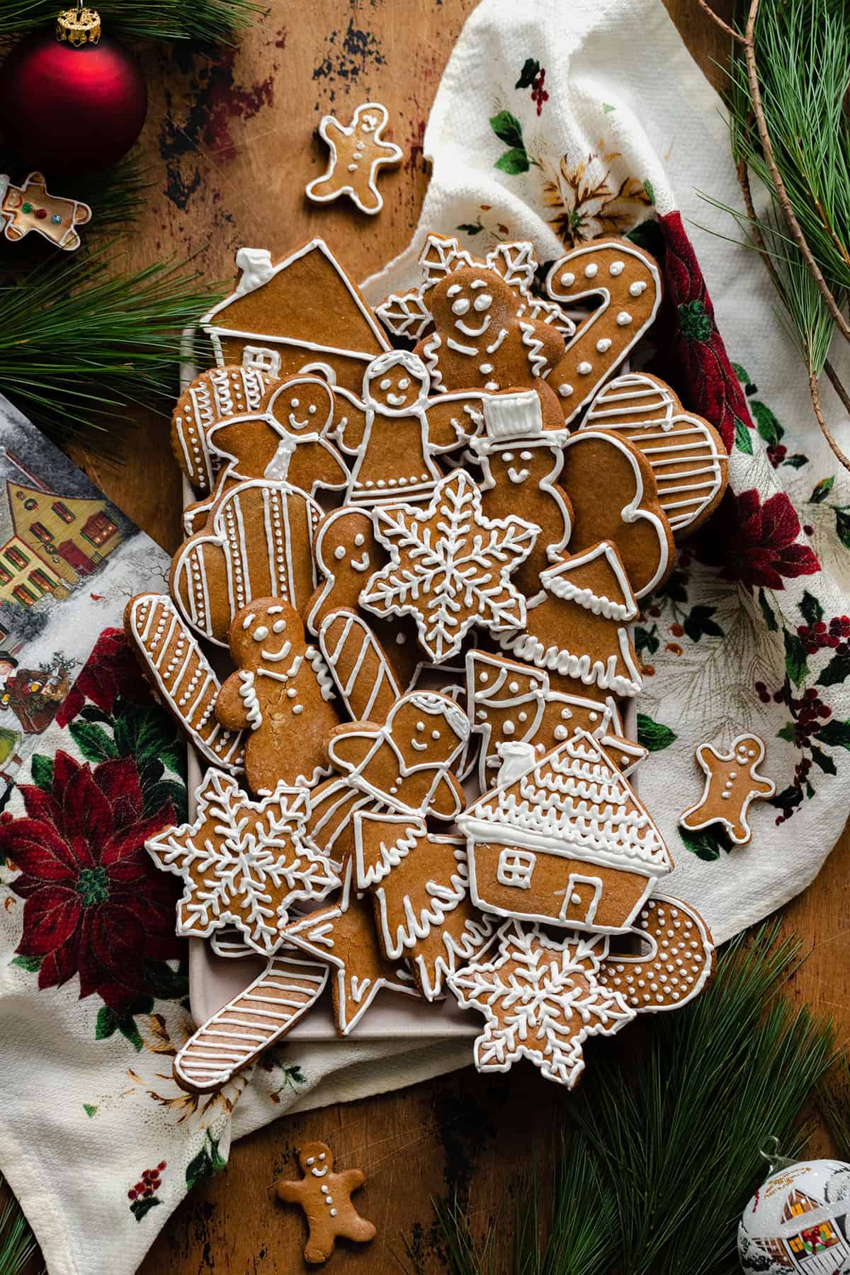 Czech Gingerbread Cookies on a plate with a Christmas tea towel underneath. On a light wooden background with pine branches and Christmas decorations around the plate.