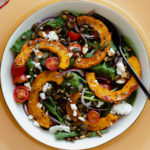 A close up of delicata squash salad in a white bowl on a decorative gold platter