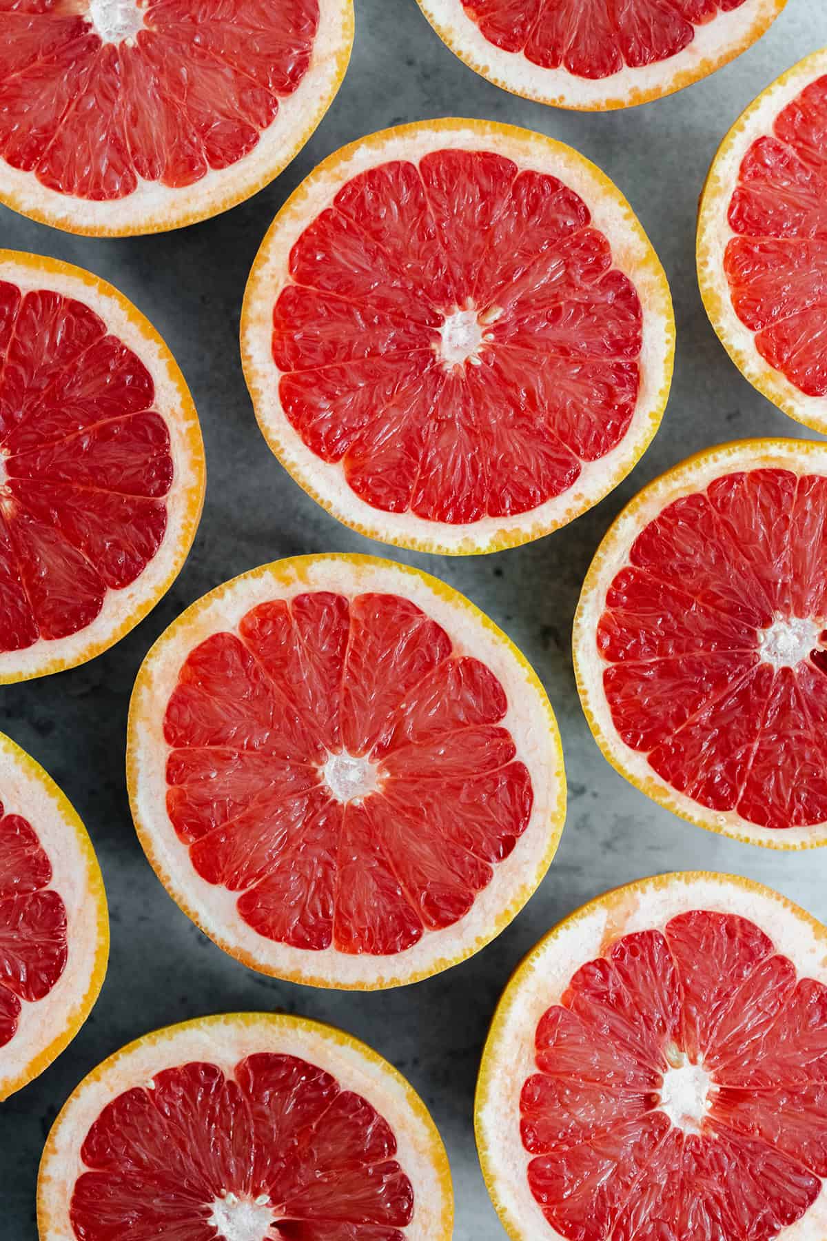 Grapefruits cut in half, laid out evenly cut side up on a gray background.