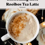 Blossoming Rose Tea Latte in a white mug with a light dusting of cinnamon on the left side. On a black table cloth with beige rose print. Fairy lights around mug. Photo contains recipe title.