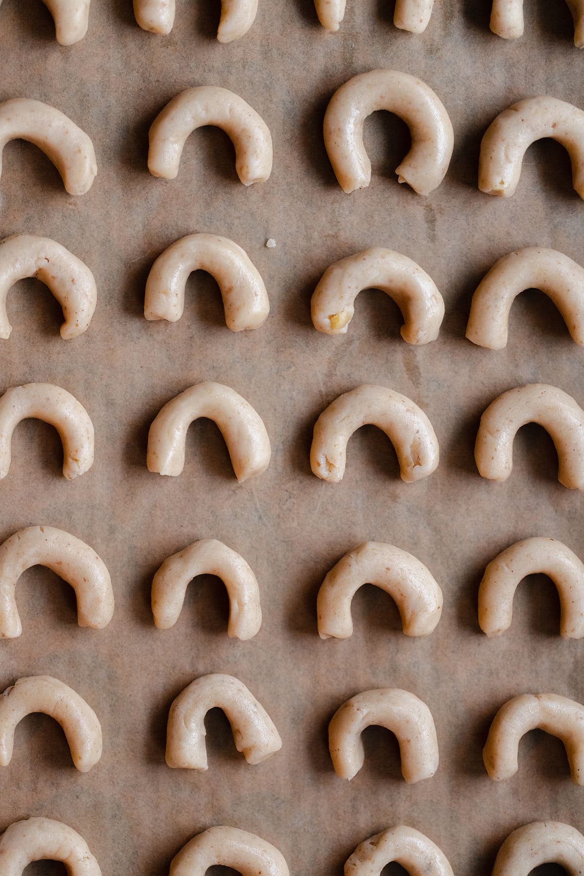 Crescent cookies shaped before baking on a baking sheet lined with baking powder.