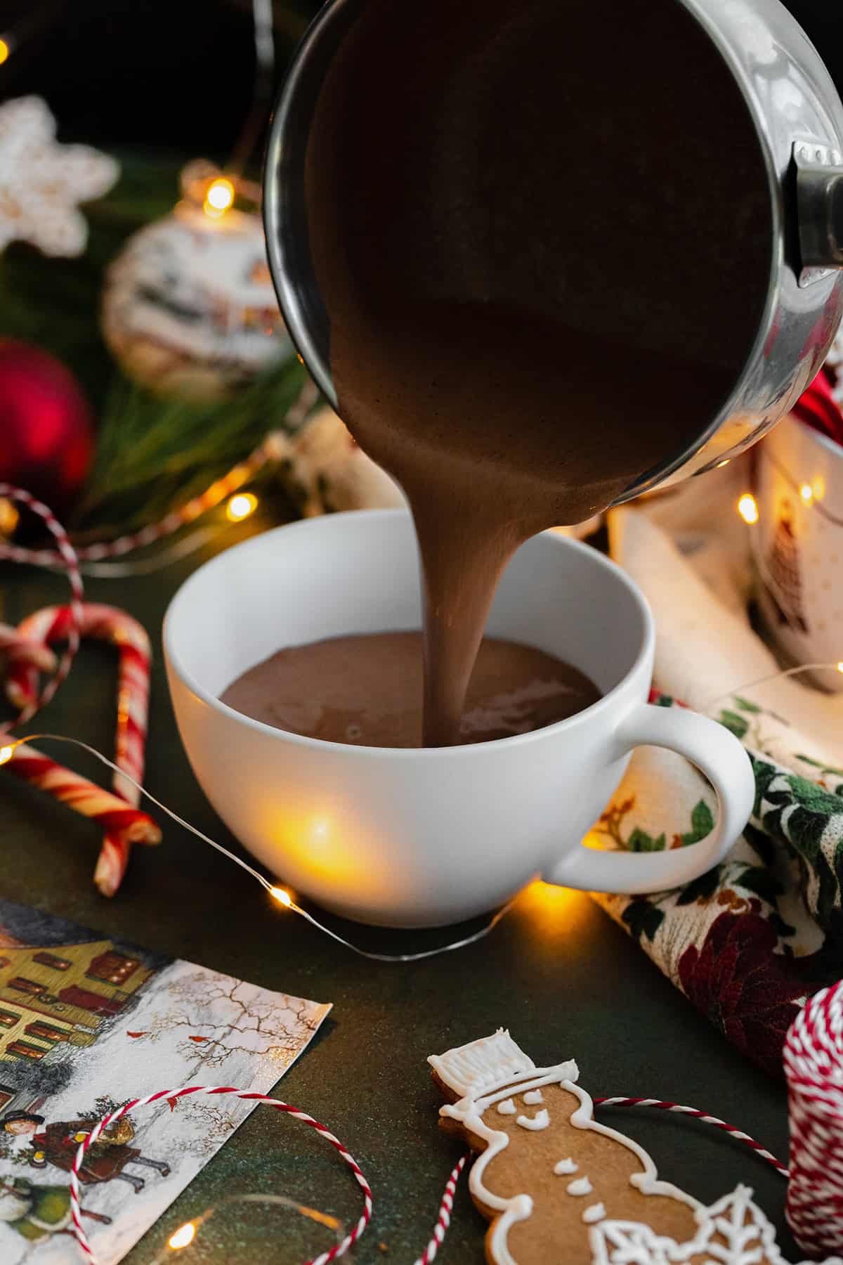 A pouring shot of hot chocolate being poured from a small pot into a white mug.