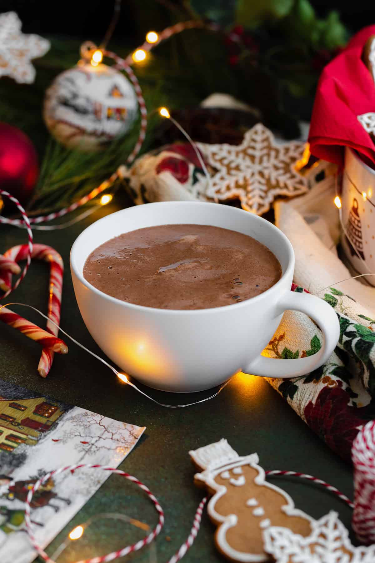 Peppermint hot chocolate in a white cup. Really creamy.Gingerbread cookies aranged around the cup. Dark green background.