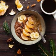 Tangerine Chocolate Chia Pudding in a bowl on a dark wooden table with a cup of coffee on the left.