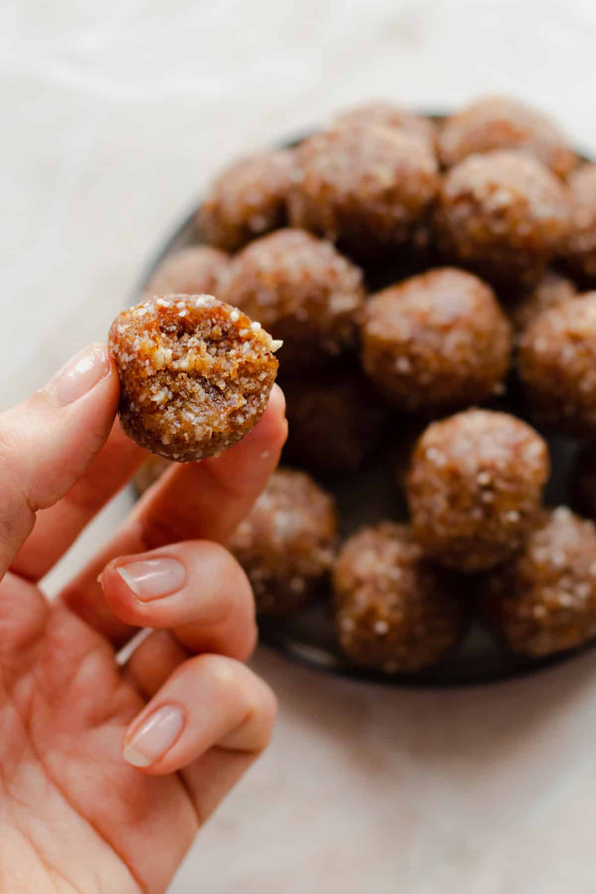 A left hand holding one energy ball on the left side of the photo. Energy ball with a bite taken out of it.