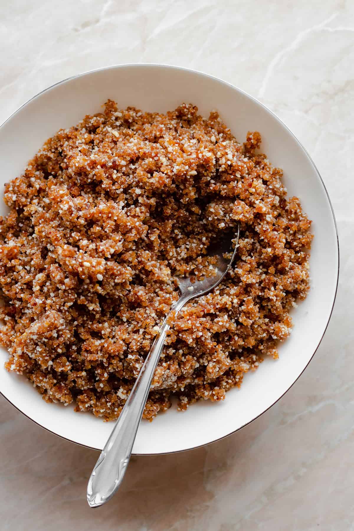 The dough for the energy balls in a white bowl with a spoon on the right side.