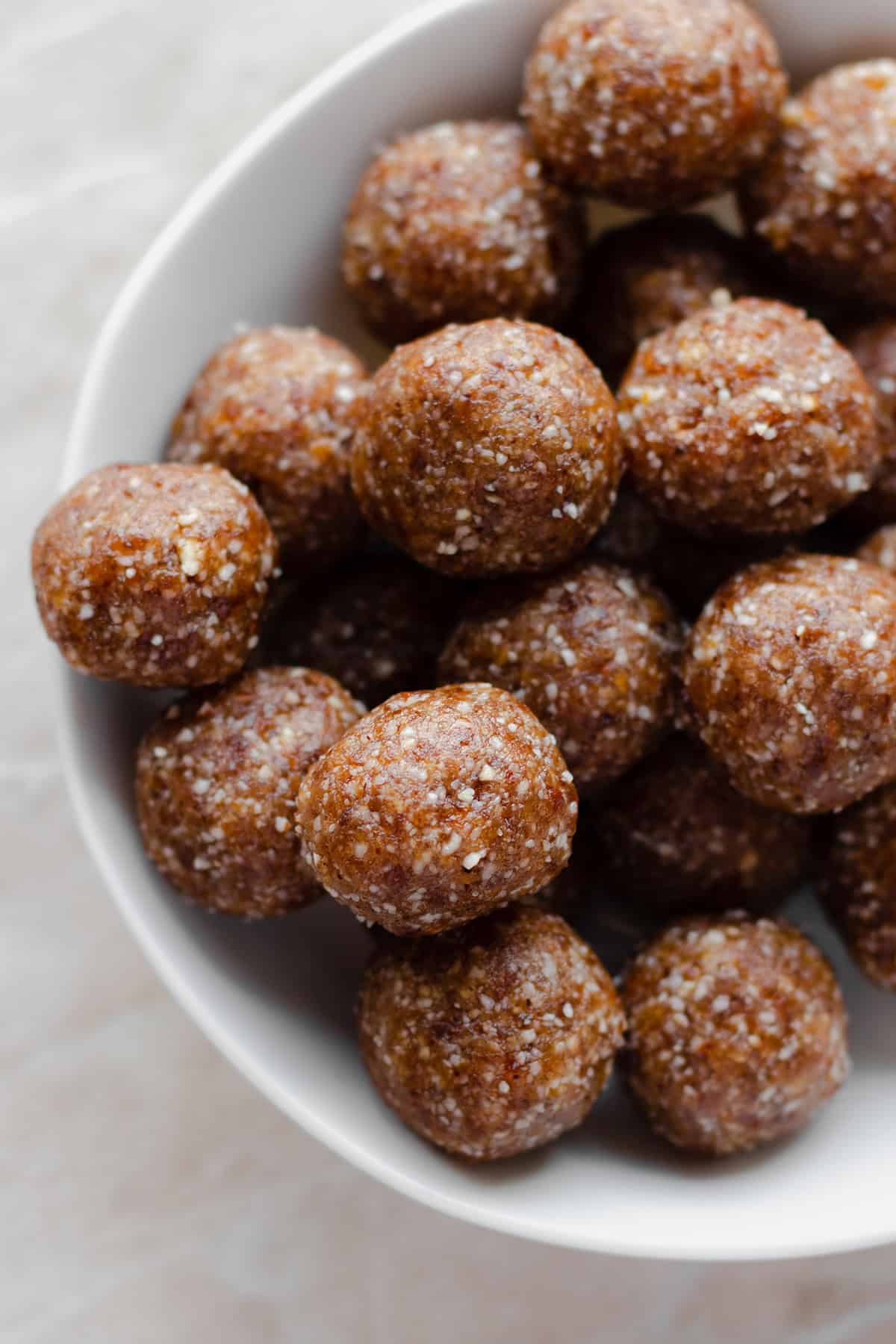 Energy balls in a white bowl on a marble counter.