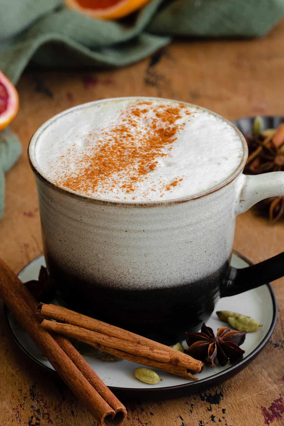 Chai Tea Latte with a sprinkle of cinnamon in a ceramic black and white mug. On a light wooden table.