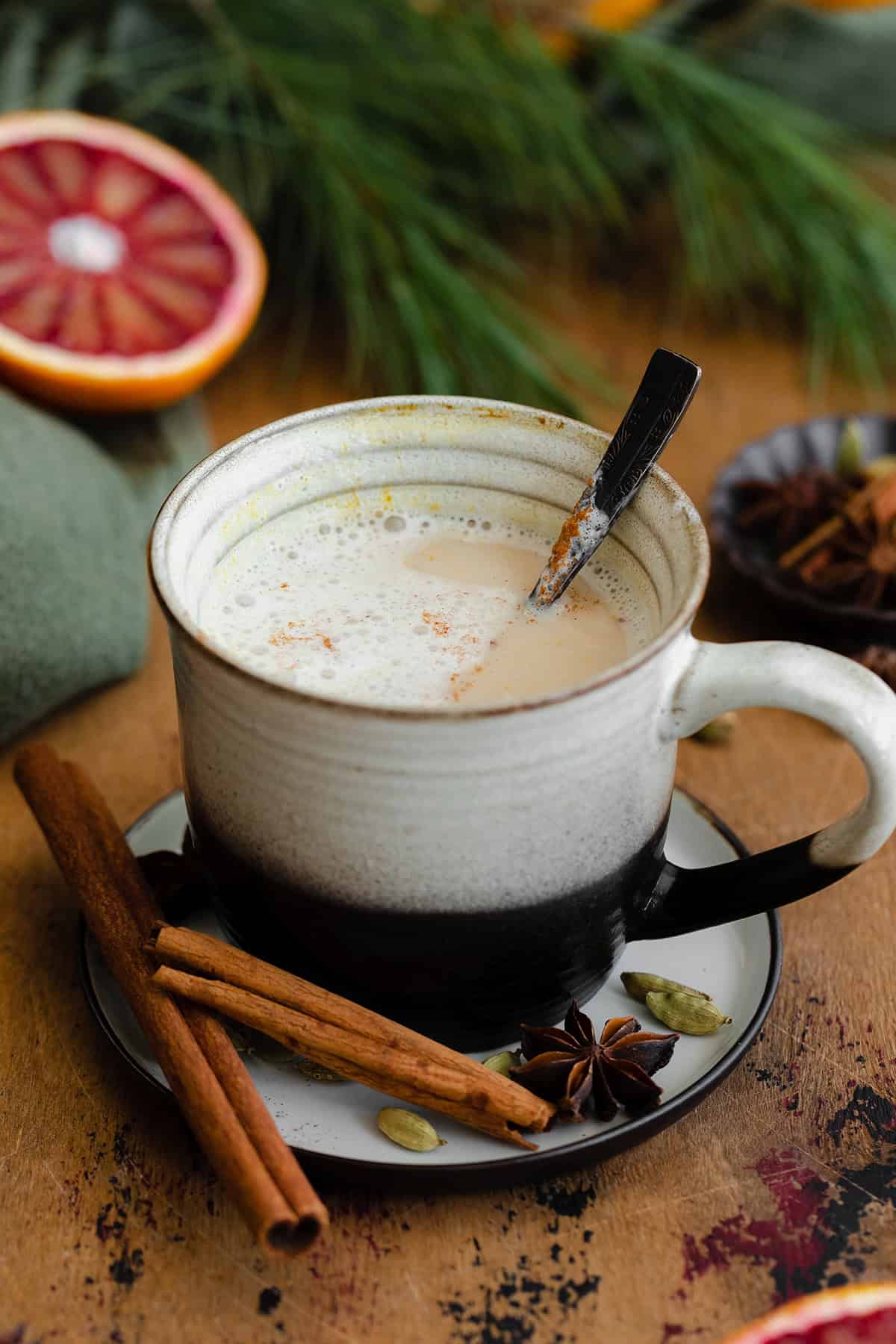 A half drunken Blood Orange Chai Tea Latte in a ceramic black and white mug. On a light wooden table with blood oranges in the background.