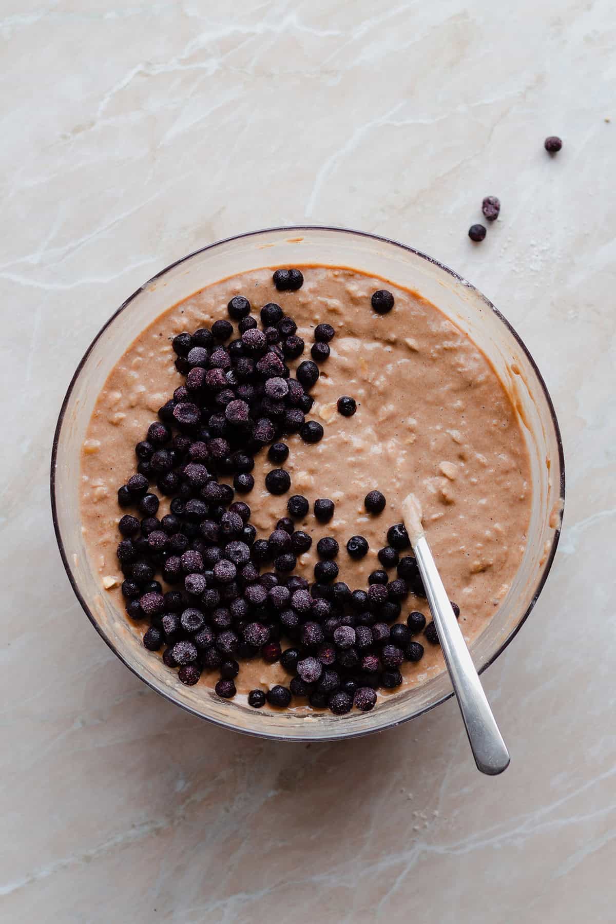 Dough for blueberry pancakes in a bowl with the frozen wild blueberries on top.