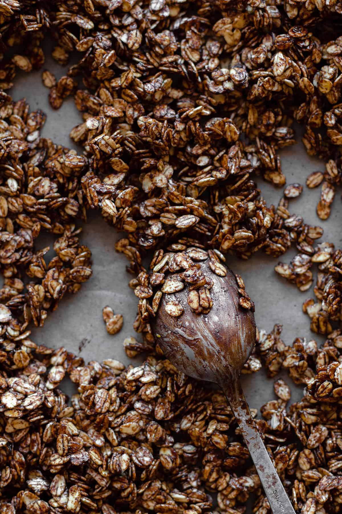 Granola before baking with a spoon covered with the oats and the carob mixture in the middle.