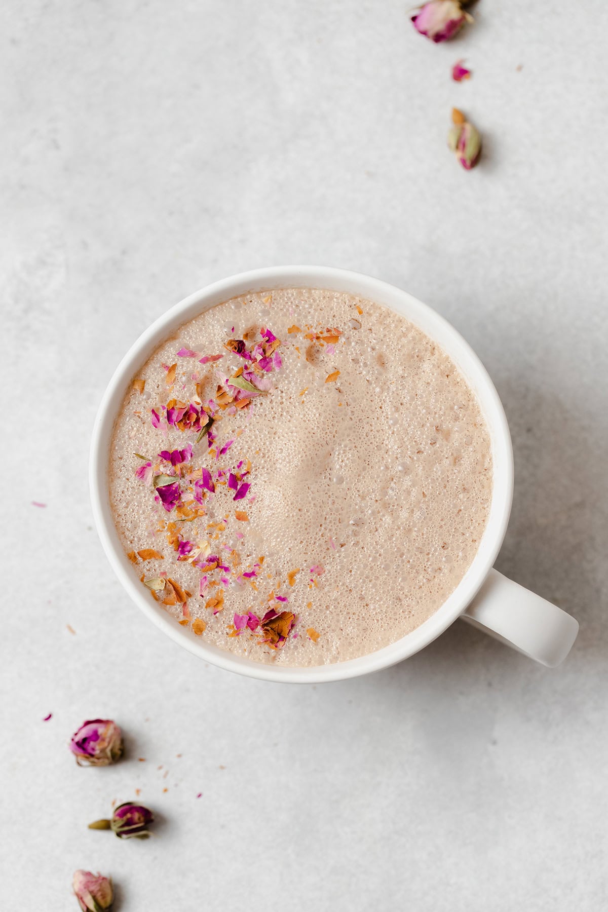 Hibiscus earl grey latte in a white mug on a light grey background. Garnished with crushed dried rose petals.