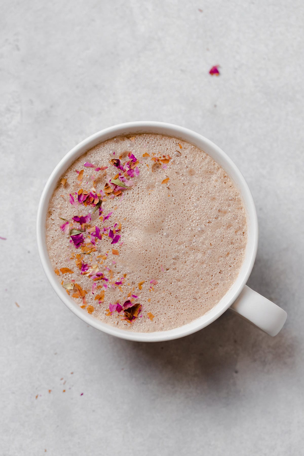 Hibiscus earl grey latte in a white mug on a light grey background. Garnished with crushed dried rose petals.