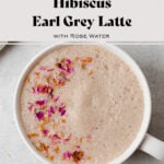 Hibiscus earl grey latte in a white mug on a light grey background. Garnished with crushed dried rose petals.