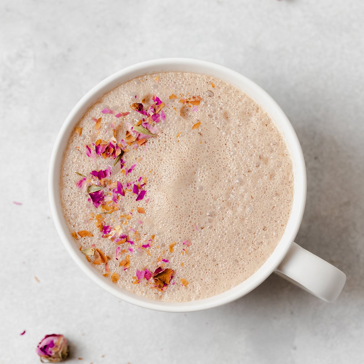 Hibiscus earl grey latte in a white mug on a light grey background. Garnished with crushed dried rose petals.