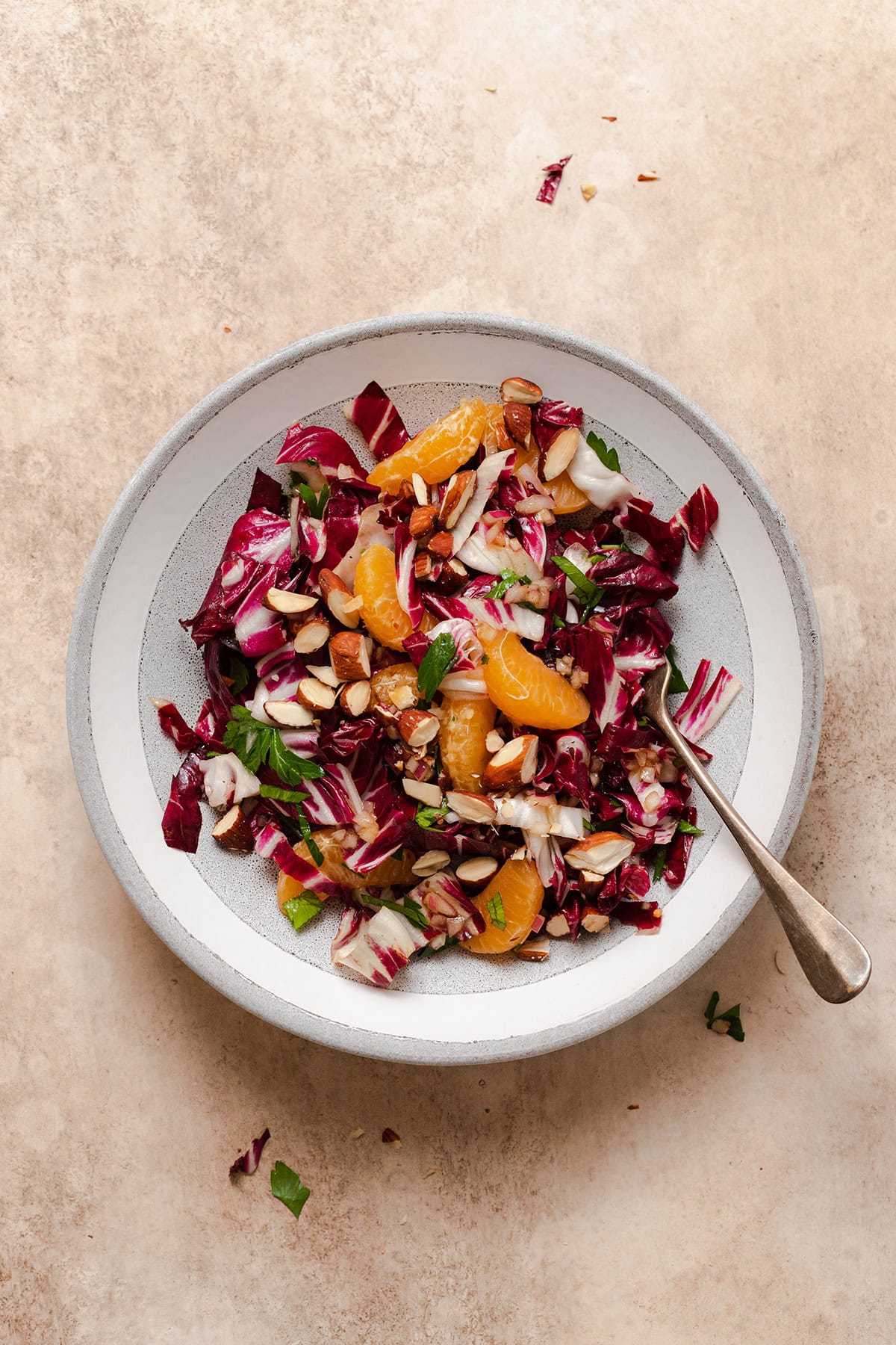 Radicchio Clementine Salad shown on a shallow grey bowl with a white stripe along the edge. Fork resting on the right side of the bowl in the salad.