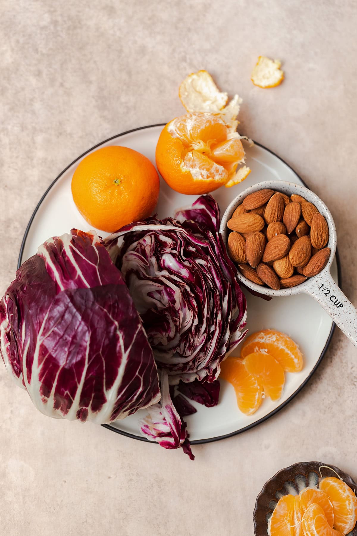 Ingredients for the clementine salad laid out on a plate. Whole clementines, whole almonds, and a whole head of radicchio.