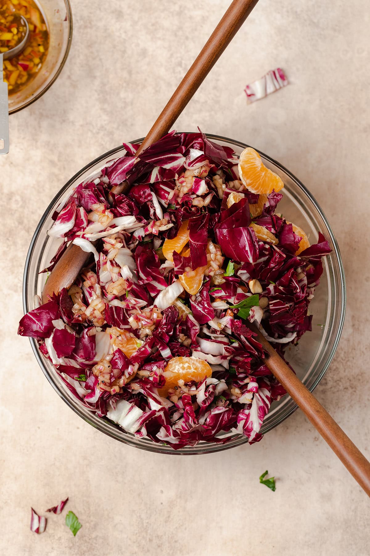 Radicchio Clementine Salad shown in a glass bowl with wooden salad spoons inserted in the bowl.