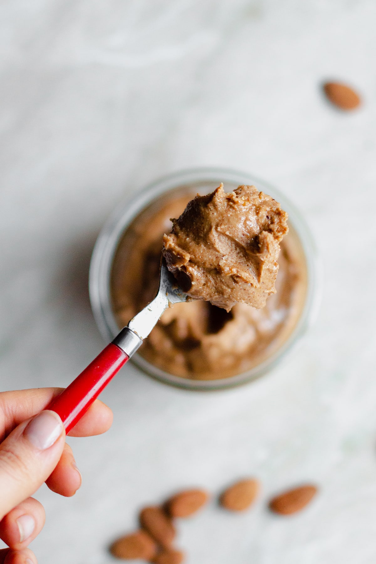 Salted Caramel Nut Butter in a glass jar with a red spoon holding a spoonful.
