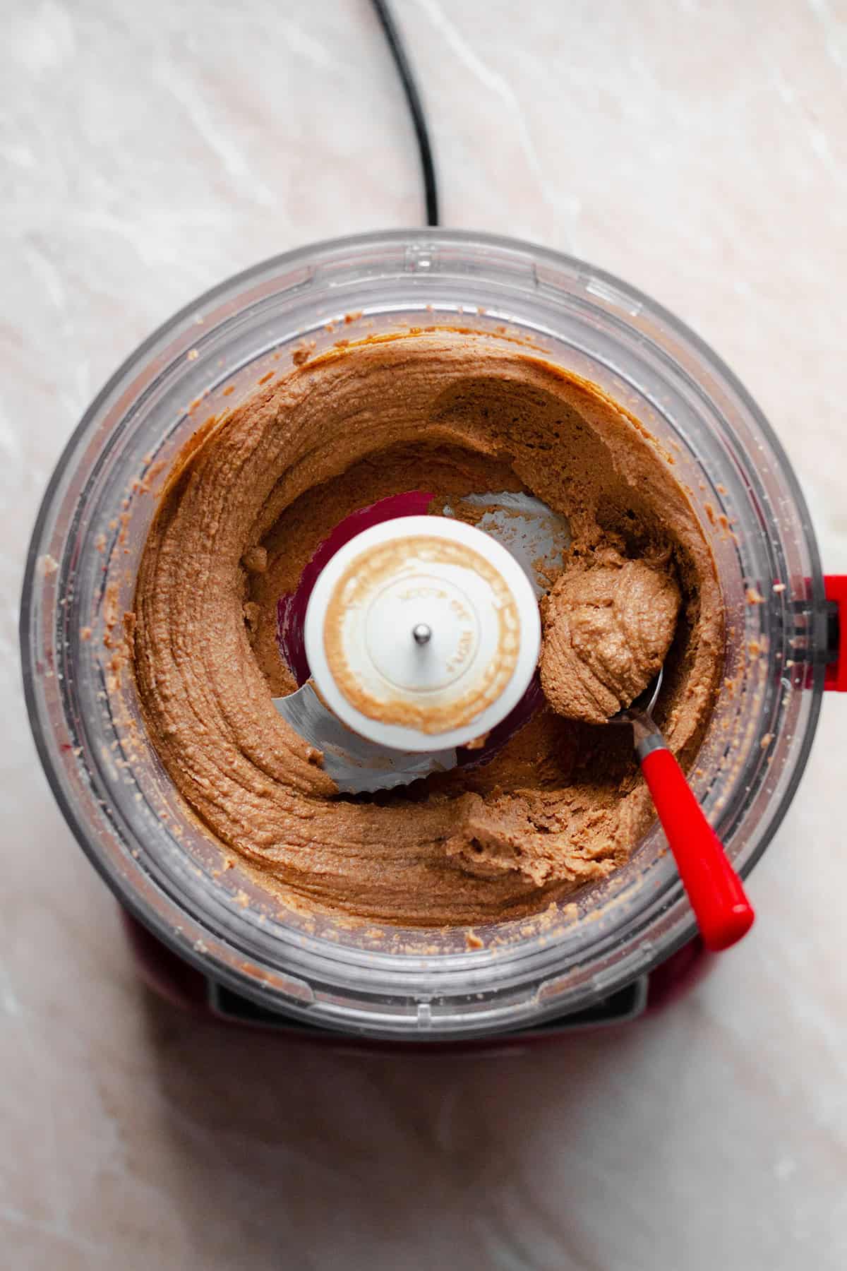 Salted Caramel Nut butter in a food processor with a red spoon on the right.