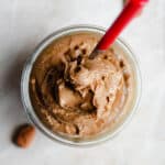 Salted Caramel Nut Butter in a glass jar with a red spoon.