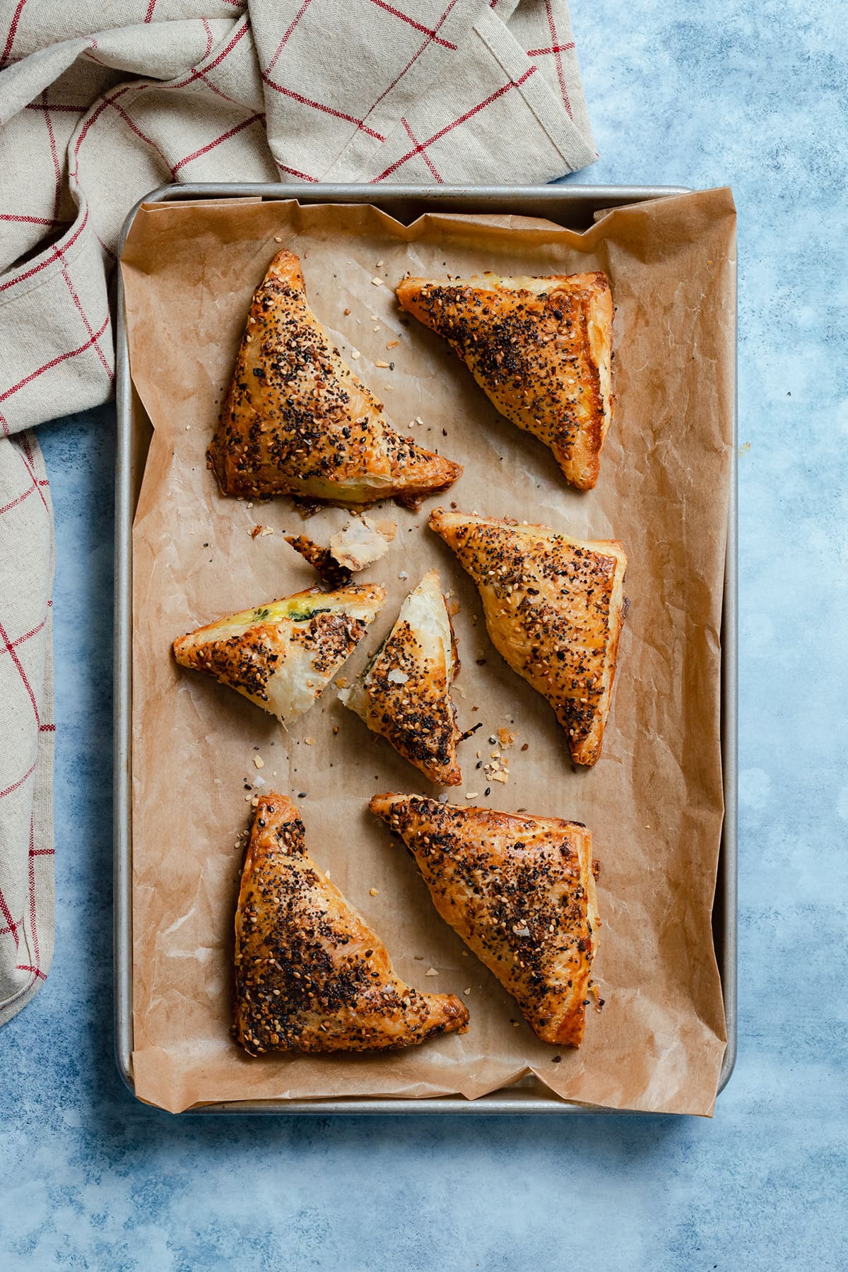 Spinach and Feta Puff Pastry Triangles on a baking sheet lined with parchment paper. One triangle cut in half in the middle of the sheet.